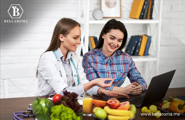 Dos mujeres leyendo en su ordenador frente a una mesa llena de frutas y vegetales